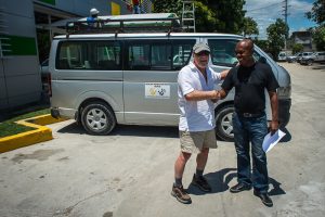 Eric shaking hands in front of a van with a Healing Hands for Haiti logo on the side